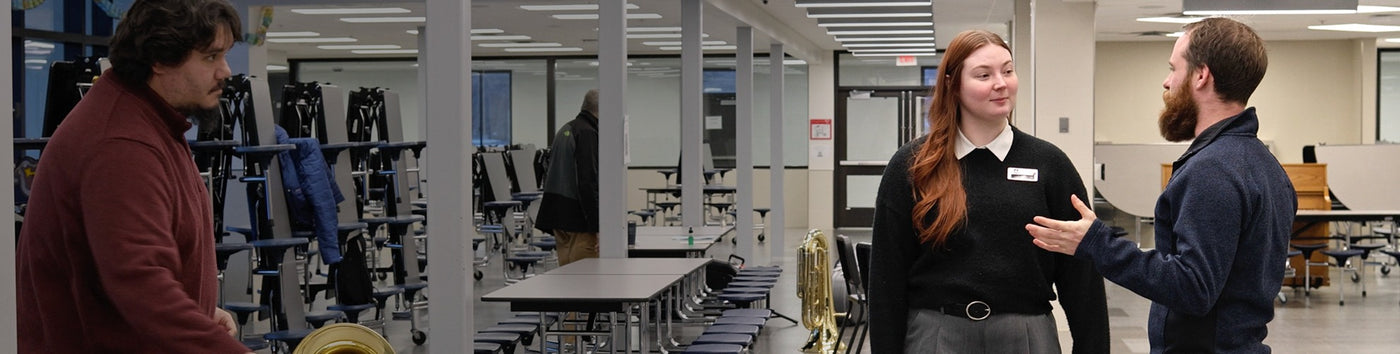 Three people in a classroom setting with desks and chairs.