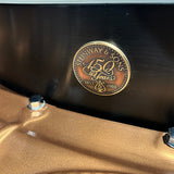Close-up of a round bronze-colored metal emblem on a dark metallic surface, featuring the text 'Steinway & Sons 150 Years 1853-2003' and a small crest below.