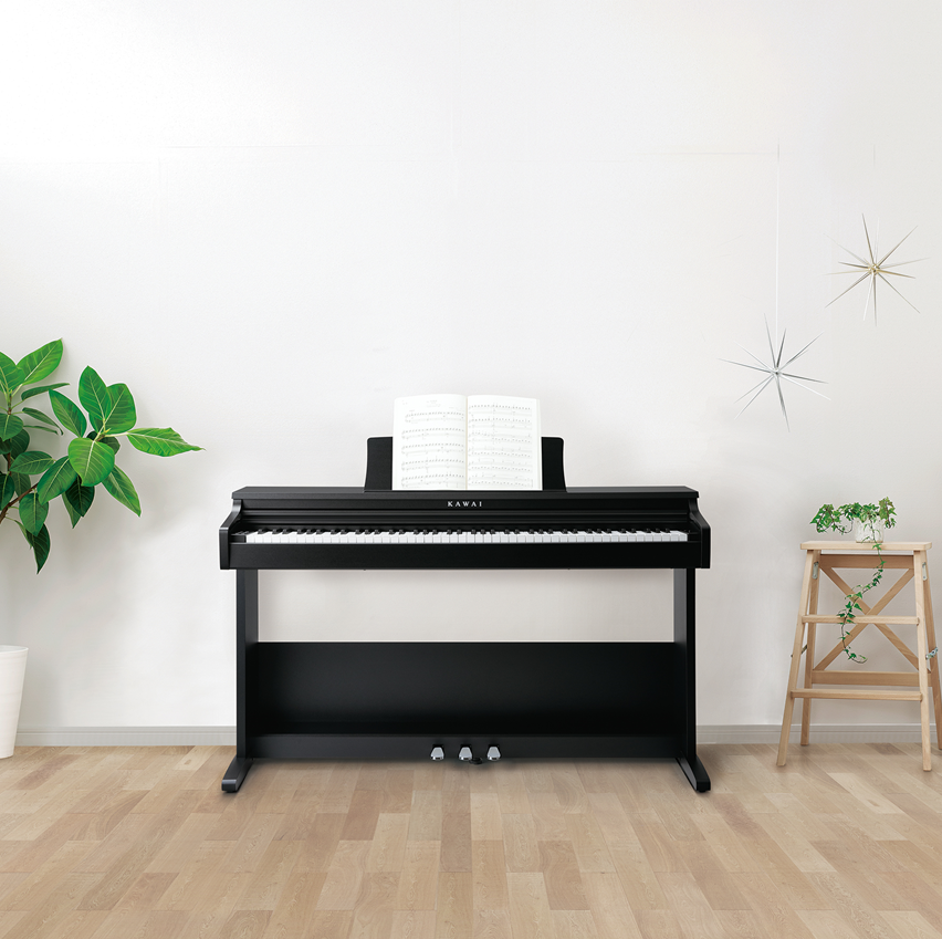 Black Kawai digital piano in a room with a plant and small table.