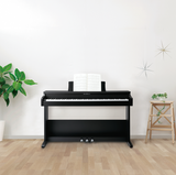 Black Kawai digital piano in a room with a plant and small table.