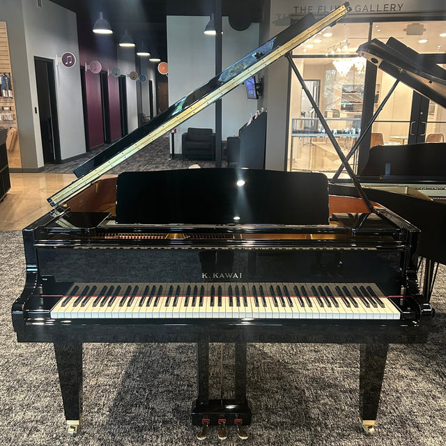 A black Kawai grand piano with its lid open, positioned on a gray patterned carpet inside a showroom or gallery.