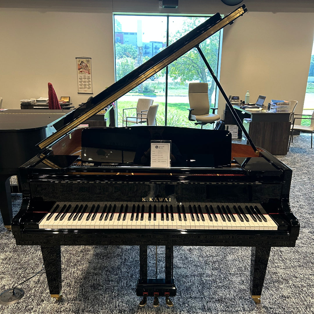 A black grand piano with the lid open, showing the keyboard and interior, photographed in a showroom with windows and chairs in the background.