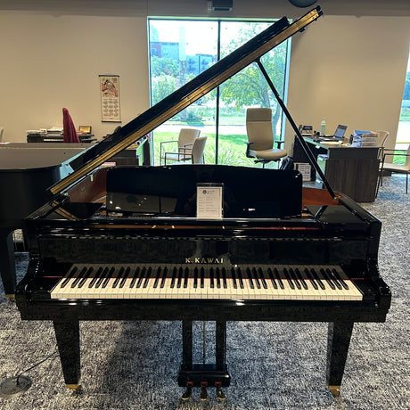 A black grand piano with the lid open, showing the keyboard and interior, photographed in a showroom with windows and chairs in the background.