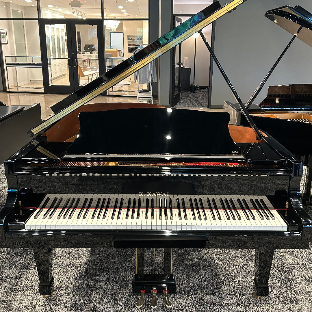 A black grand piano with its lid open, showing the keyboard and inner structure, photographed in a showroom or gallery interior with other pianos and glass doors in the background.