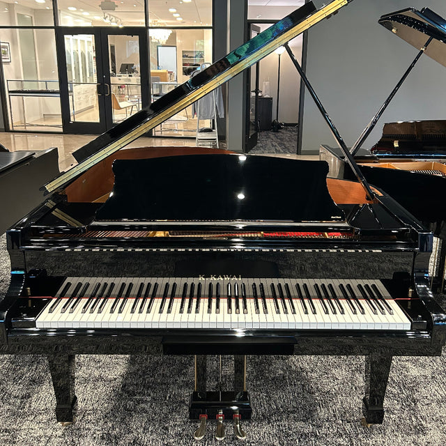 A black grand piano with its lid open, showing the keyboard and inner structure, photographed in a showroom or gallery interior with other pianos and glass doors in the background.