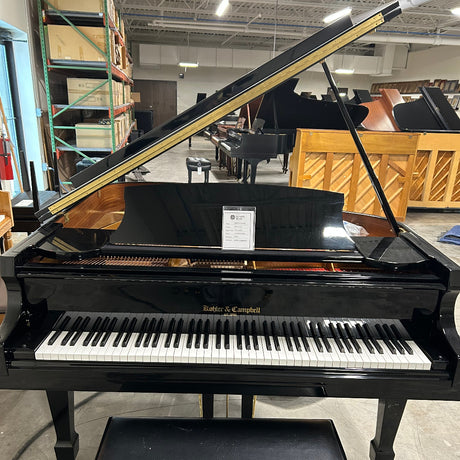 Black upright piano in a storage or warehouse setting with visible labels.