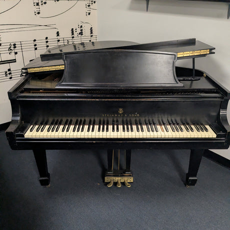 Black grand piano in a room with sheet music on the wall.