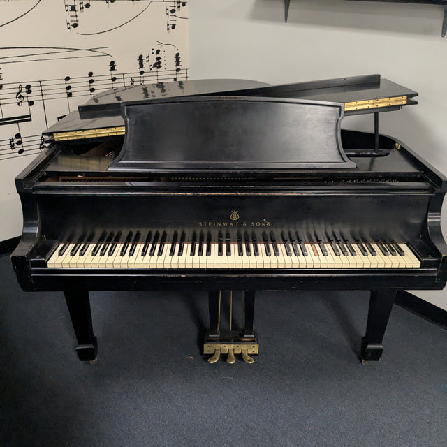 Black grand piano in a room with sheet music on the wall.