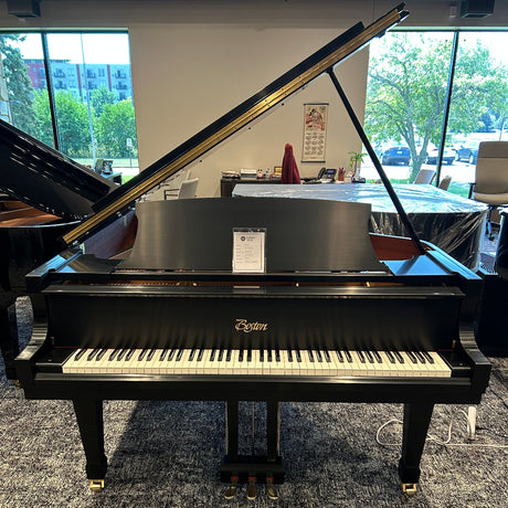 A black Boston grand piano with the lid open, photographed indoors in a showroom with large windows and other pianos visible in the background.
