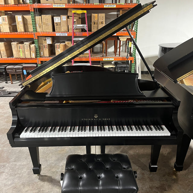 Black grand piano with a bench in a storage or warehouse setting