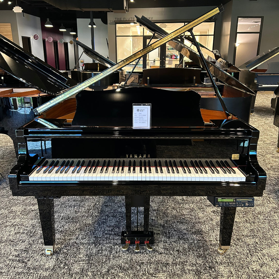 A black grand piano with its lid open, positioned in a showroom with other pianos and musical instruments visible in the background.