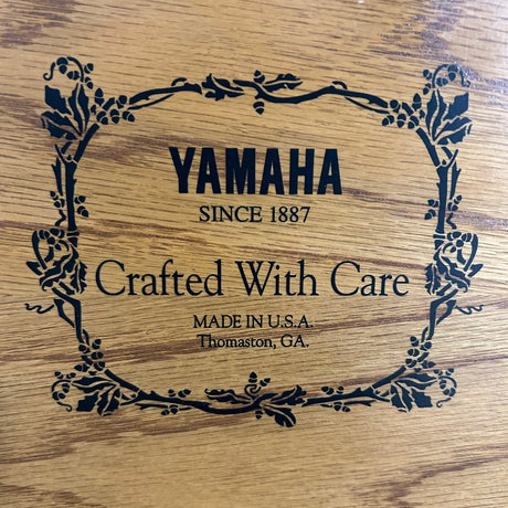 Close-up of a wooden surface with black printed Yamaha branding and decorative border text reading 'Yamaha Since 1887', 'Crafted With Care', and 'Made in U.S.